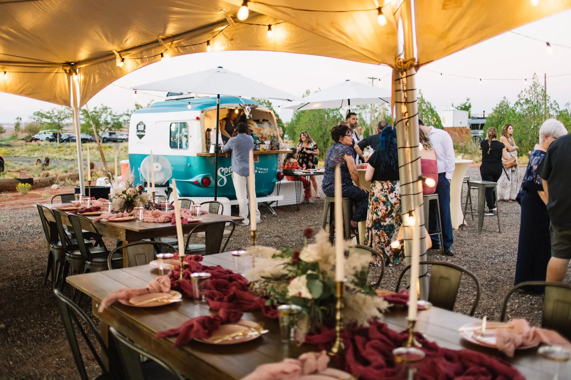Outdoor gathering under string lights with tables, chairs, and a food truck in the background, with people socializing and enjoying the event.